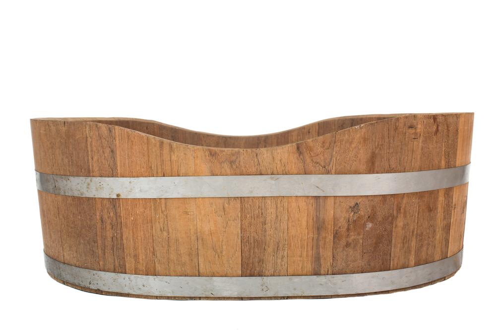 An empty wooden barrel or tub, viewed from the side. The top edge of the barrel features a wave-like, scalloped pattern, with the sides rising and falling in smooth curves.